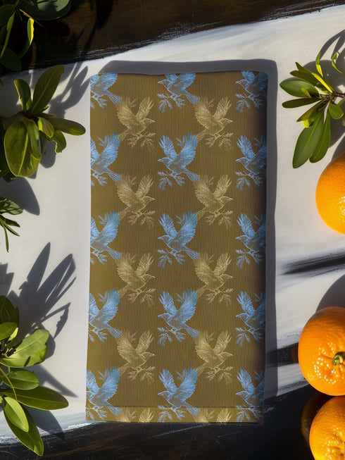 Set of four golden cloth napkins featuring alternating powder blue and metallic gold ravens in flight, sized 18x18 inches.